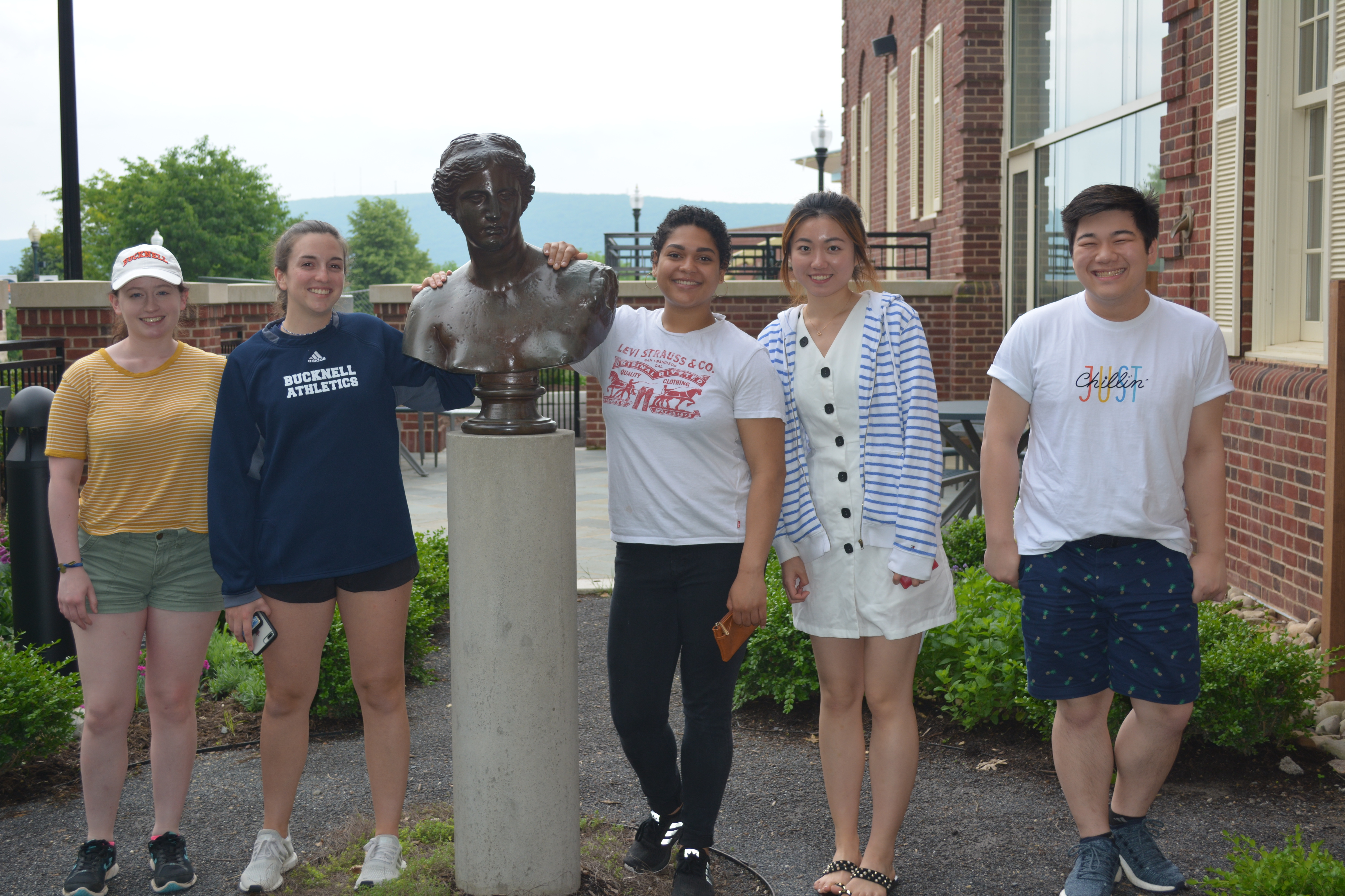 Five students smiling and standing the the bust in the Hildreth-Mirza Hall courtyard.